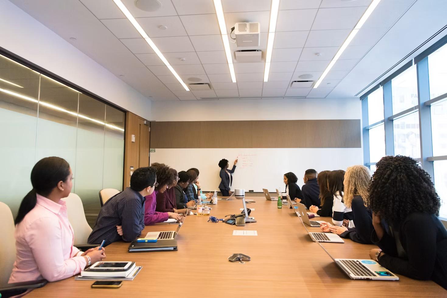 An African team strategising in a boardroom while a woman explains ideas on a whiteboard